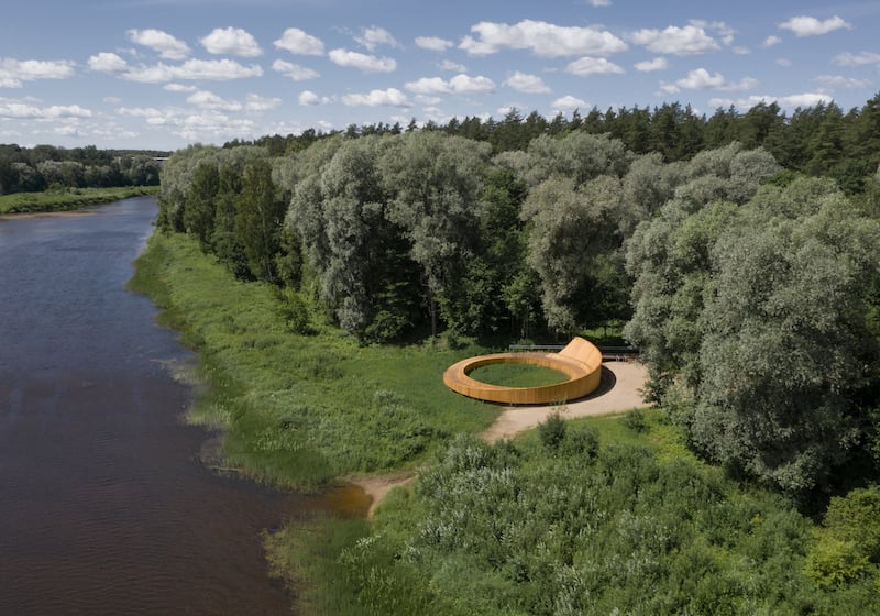 This curved wooden terrace carves an elegant path through Latvia's picturesque forest