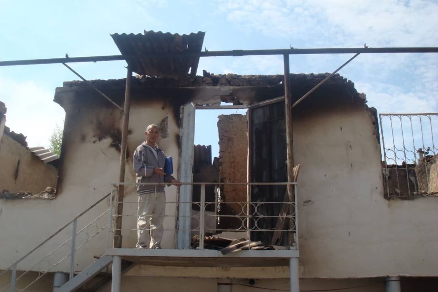 Azimjan standing in front of a burned house following the 2010 South Kyrgyzstan ethnic clashes.
