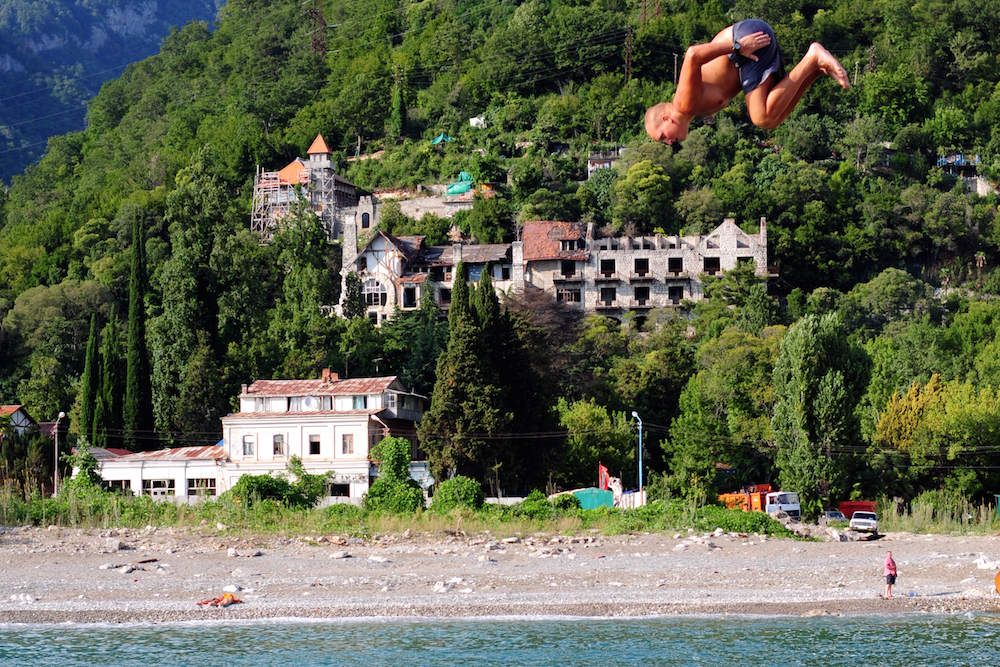 A man dives into the sea at Gagra in Abkhazia, with ruined sanitoria in the background. Image: mikesub under a CC licence