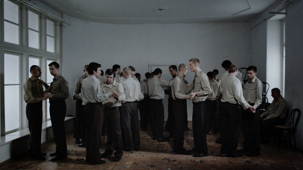 Still from the Celebration video, 2014. In this video, we see a group of identically dressed men dancing together indifferently. Here, Kanis explores the ways in which oppression by the states makes it into our everyday lives