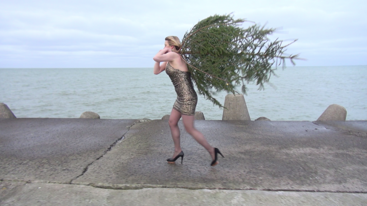 Personal Christmas, 2020. Holidays can be an especially lonely time. In this performance, a woman in a golden dress carries a Christmas tree on her own, walking along the seashore and through the empty night city